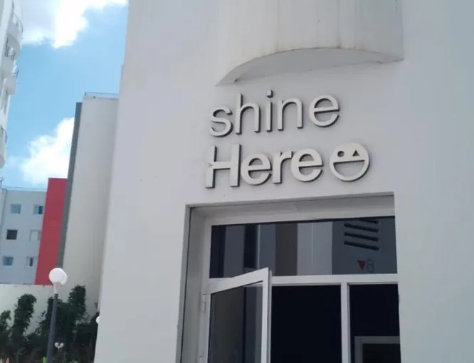 Lettres en relief Shine Here sur façade blanche